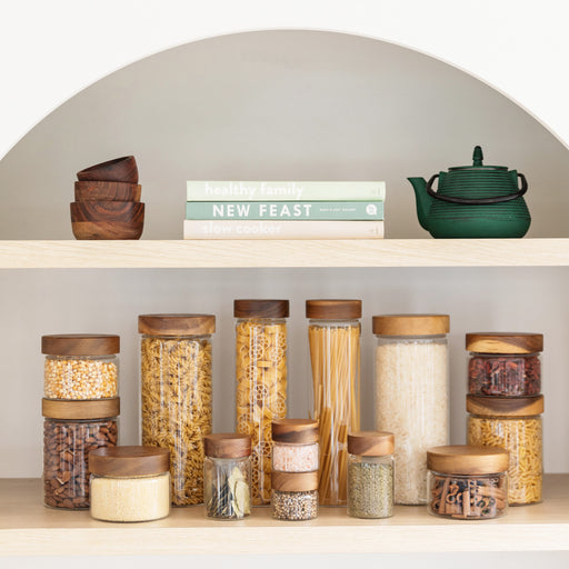 Set of glass jars with wooden lids on a shelf with books and a teapot.